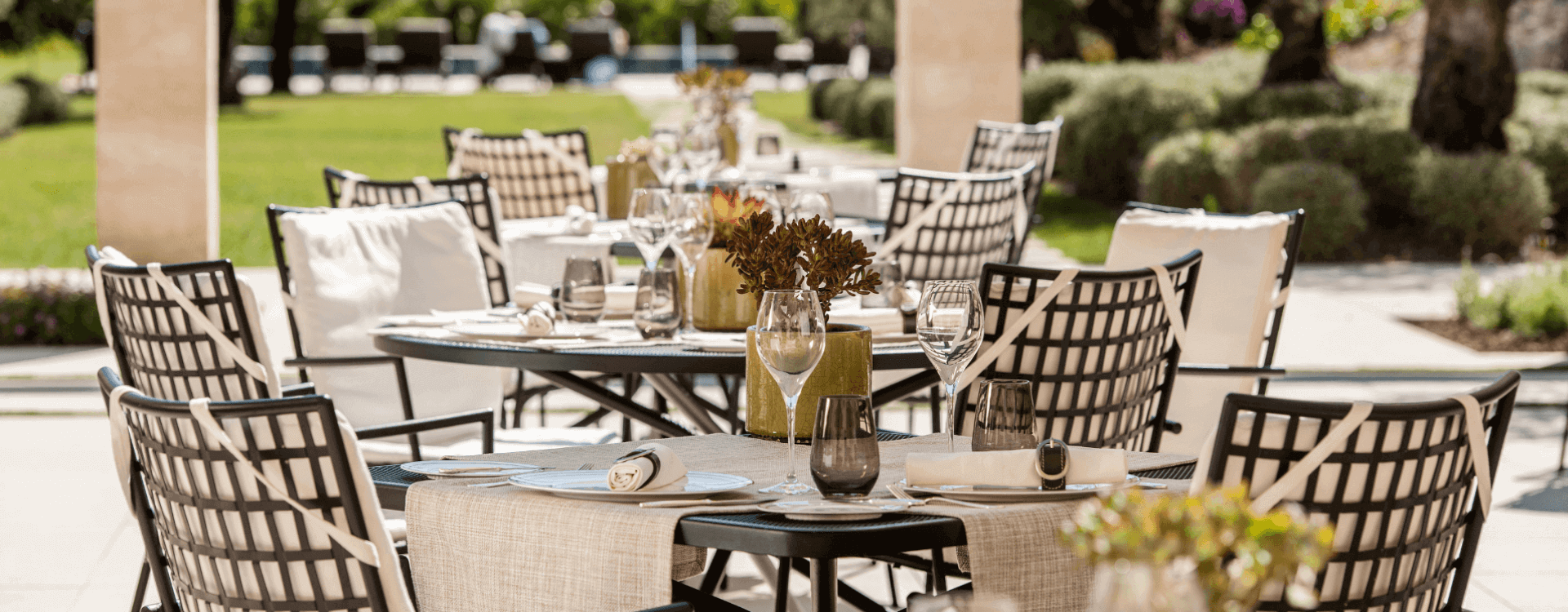 Several small tables set with plates, wine glasses, water glasses and flowers in the garden of the Hotel Castell Son Claret in Mallorca.
